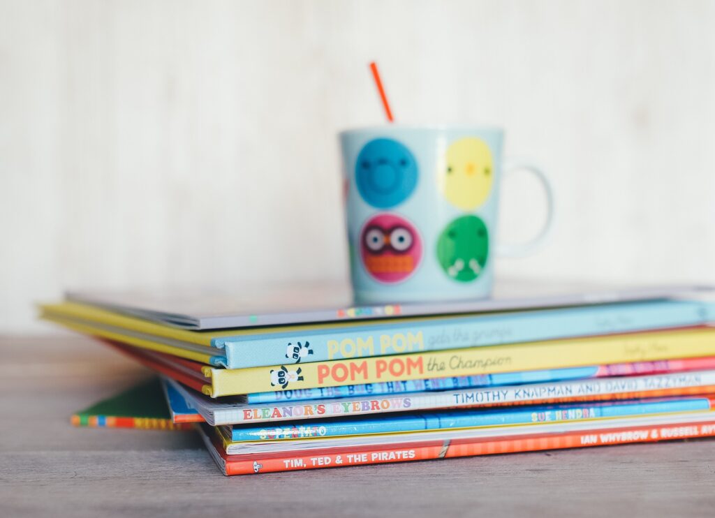 Materiale scolastico: libri per bambini ripresi di costa con tazza da colazione colorata sullo sfondo.